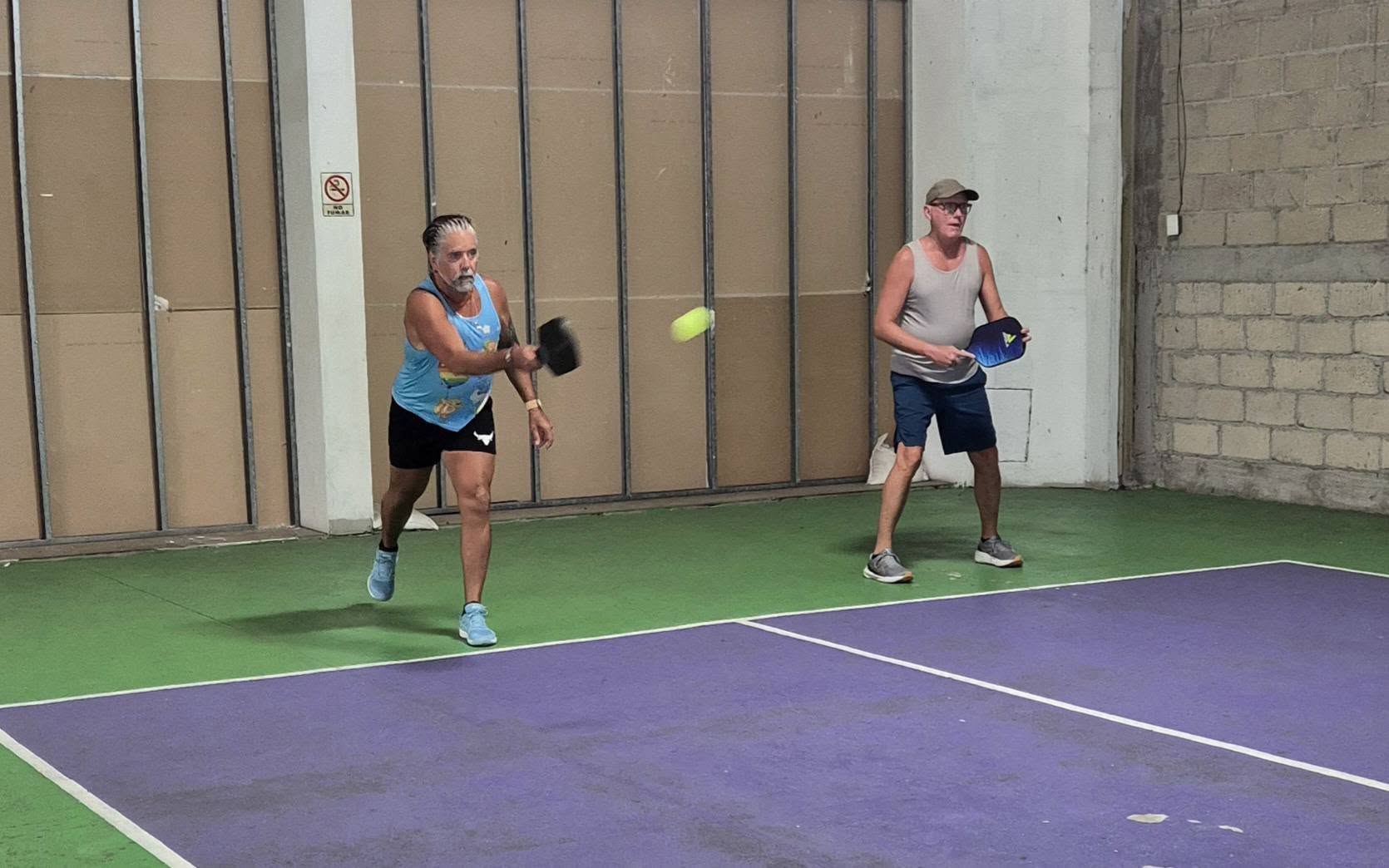 Two players mid-rally on the purple and green indoor courts at Puerto Mágico